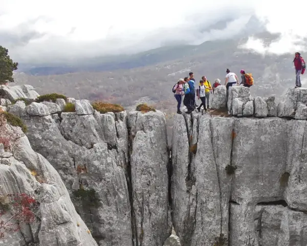 Grupa turystów na skalnym szczycie, podziwiająca widok na góry. Może to być okolica stolicy Czarnogóry, Podgoricy.