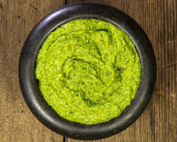Pesto genovese ricetta originale in un mortaio di pietra, su un tavolo di legno rustico. Fresco e profumato.