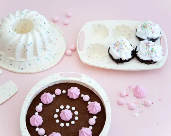 Förberedelser för ett härligt baka kalas! En sockerkaksform, muffinsform och en färdig chokladkaka med rosa maränger och strössel.