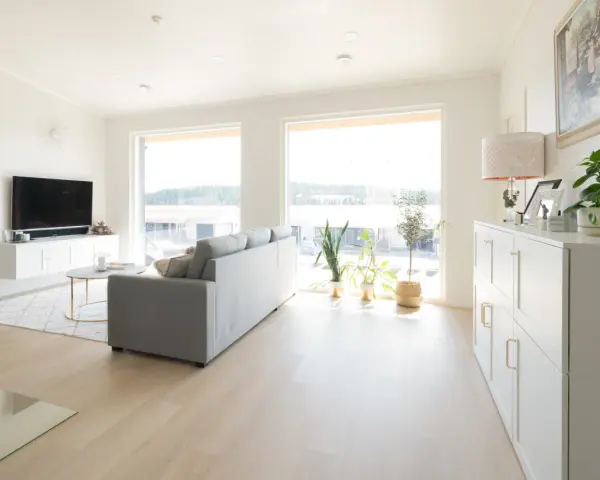 Ett ljust vardagsrum med en grå soffa, ett runt soffbord och en vit förvaringsmöbel. En lampa med vitt ljus lyser upp rummet.