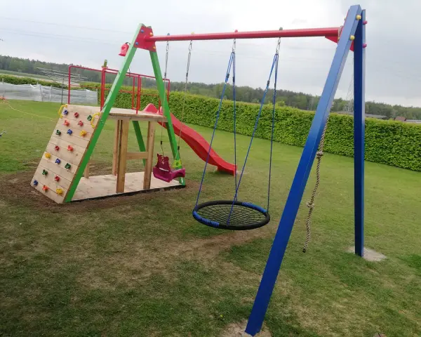 Plac zabaw z wspinaczką, zjeżdżalnią, huśtawkami i okrągłą huśtawką.