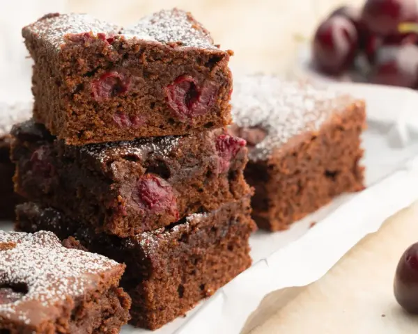 Saftige Stücke von Omas Schoko-Kirsch-Kuchen, bestäubt mit Puderzucker. Kirschen sind im dunklen Teig sichtbar.