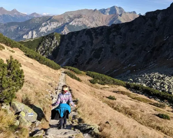 Osoba wędruje kamienistym szlakiem w Tatrach. Widok na góry i dolinę, idealne tatry szlaki dla średnio zaawansowanych.