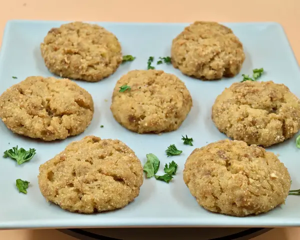 Sei polpette di patate dorate e croccanti, guarnite con prezzemolo fresco, su un piatto azzurro.
