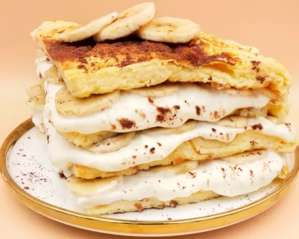 Wysoki omlet z bananem, przełożony kremem i plasterkami banana, posypany kakao. Pyszny deser na talerzyku.