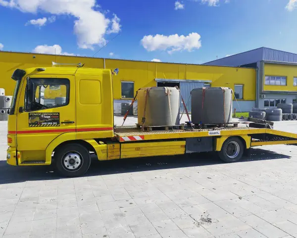 Żółta laweta z dwoma betonowymi elementami, gotowa do transportu. To **assistance warta** uwagi, gdy potrzebujesz przewieźć ciężkie ładunki.
