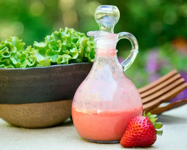 Erdbeeren mit Balsamico-Dressing in einer Karaffe, daneben eine Schüssel Salat und eine einzelne Erdbeere.