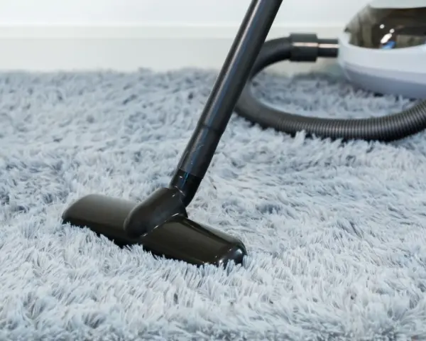 Vacuum cleaner head on a fluffy grey rug, demonstrating how to wash a rug by removing dust and debris.