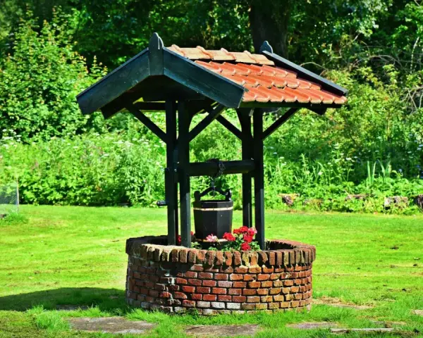 Un puits de briques rouges, orné de fleurs, avec un seau suspendu, prêt à creuser un puits pour abreuver le jardin verdoyant.