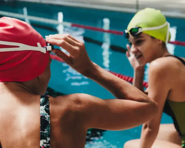 Deux nageuses se préparent pour une course de nage brasse. L'une ajuste ses lunettes, l'autre sourit.
