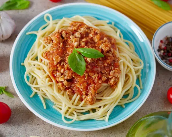 Pyszny, prosty sos do spaghetti z mielonym mięsem i pomidorami, udekorowany bazylią. Obok czosnek, pomidorki i kolorowy pieprz.