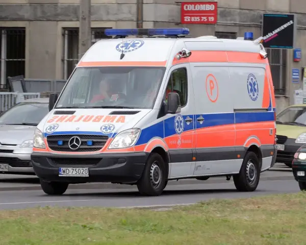 Karetka na sygnale z oznaczeniami medycznymi, jadąca ulicą.
