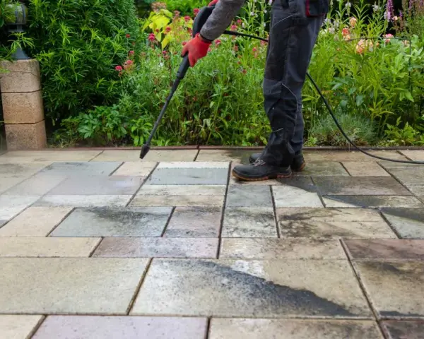 Persona con guantes rojos usa hidrolimpiadora para limpiar suelo terraza exterior.