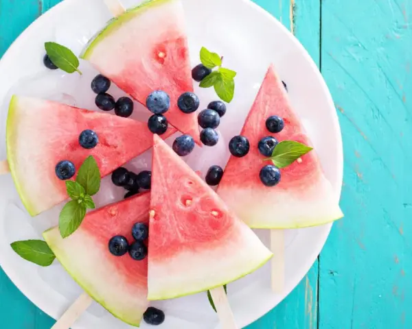 Erfrischendes Wassermelonen Eis mit Blaubeeren und Minze auf Eiswürfeln, serviert auf einem weißen Teller.