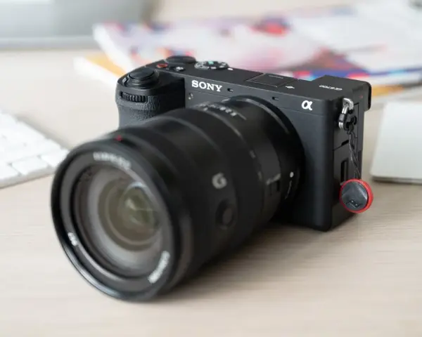 Appareil photo Sony Alpha a6700 prêt pour un test. Un objectif noir est monté, avec un clavier blanc et des documents flous en arrière-plan.