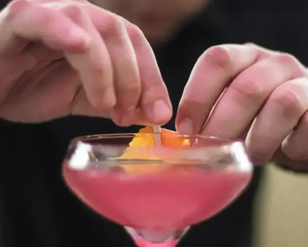 Ręce dekorują drinka skórką pomarańczy. To ostatni krok w przygotowaniu Cosmopolitan przepis.
