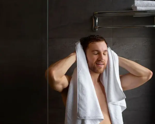Uomo si asciuga i capelli con un asciugamano bianco. Peccato che non arriva acqua calda solo nella doccia, altrimenti sarebbe stato un bagno perfetto.