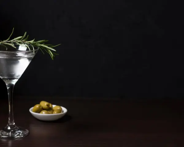 Elegancki kieliszek z drinkiem, gałązka rozmarynu i oliwki. Czy to Dirty Martini, czy klasyczne Dry Martini?