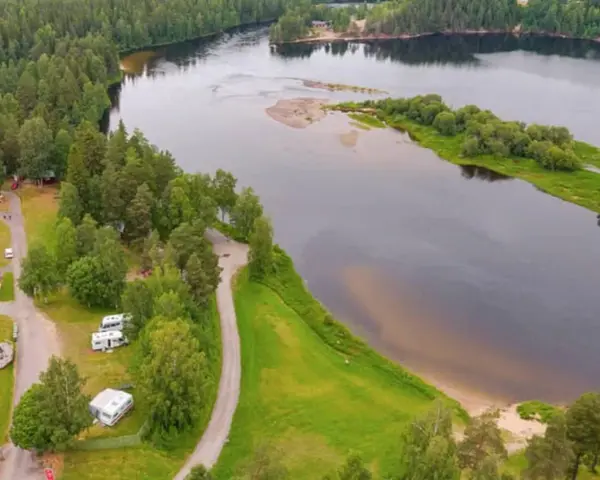 Vacker vy över Selholmens camping med husbilar och stugor vid en sjö omgiven av skog.