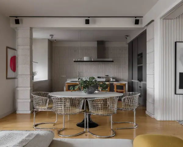 Nowoczesne wnętrze z okrągłym stołem i krzesłami w stylu bauhaus. W tle kuchnia i abstrakcyjne obrazy.