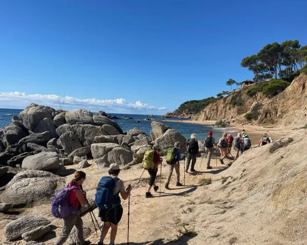 Une randonnée côtière ensoleillée, avec un groupe de randonneurs profitant d'une marche afghane le long d'une plage rocheuse et d'une falaise verdoyante.