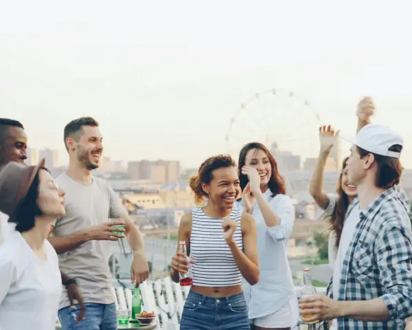 Un groupe d'amis souriants et dansant sur un toit, avec une grande roue en arrière-plan.