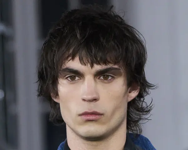 Joven con un corte de pelo mullet desordenado, mirada intensa y cejas marcadas.