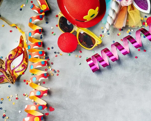 Karneval am Donnerstag: Goldene Maske, bunte Luftschlangen, rote Clownsnase und Konfetti laden zum Feiern ein.