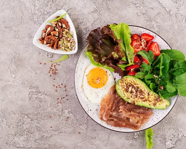 Śniadanie LCHF: jajko sadzone, boczek, awokado, sałatka z truskawkami i orzechy. Idealne na początek dnia, gdy zastanawiasz się lchf co to.