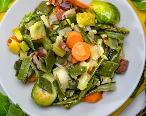 Menestra de verduras variadas con trozos de jamón en un plato blanco.
