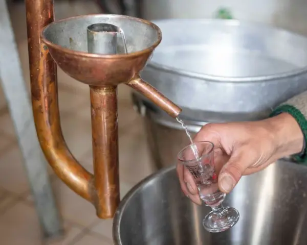 Ein Schnaps wird in ein Glas destilliert. Die Kupferapparatur zeigt, wie man Schnaps brennt.