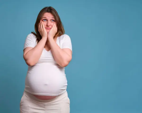 Donna incinta con le mani sul viso esprime paura in gravidanza, preoccupata per il futuro.