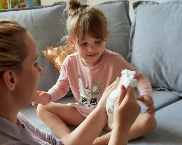 Mama pokazuje córce pieluchę, symbolizując etap, kiedy dziecko przestaje nosić pieluchy.