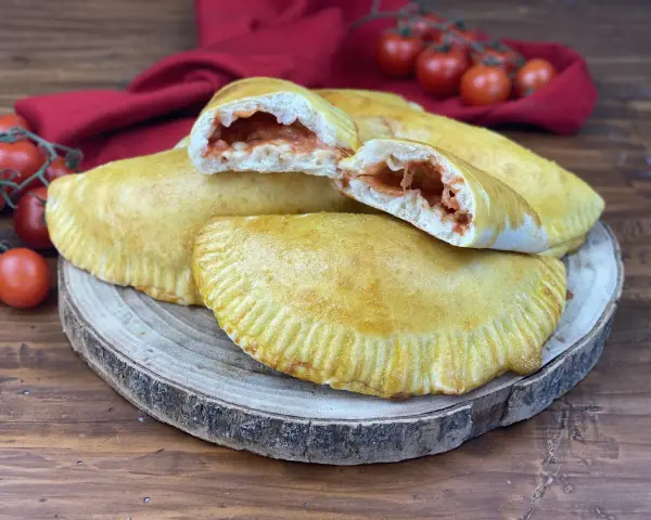 Panzerotti al forno dorati e ripieni di pomodoro e mozzarella filante, pronti per essere gustati.