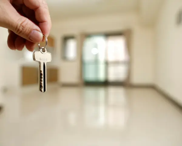 Mano sosteniendo una llave plateada frente a una habitación vacía y desenfocada.