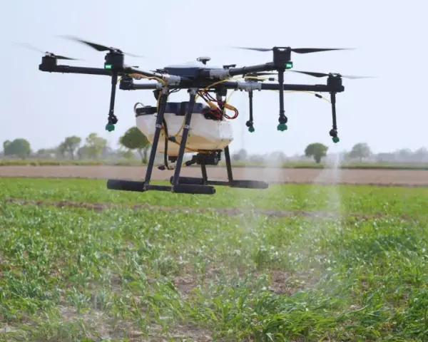 A drone sprayer, one of the types of drones in agriculture, hovers over a field, dispensing liquid onto crops.
