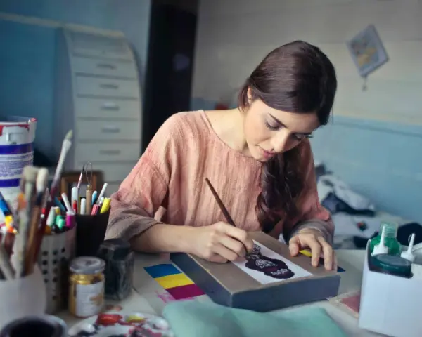 Une jeune femme se déclare artiste libre, concentrée sur sa toile, entourée de pinceaux et de peintures.
