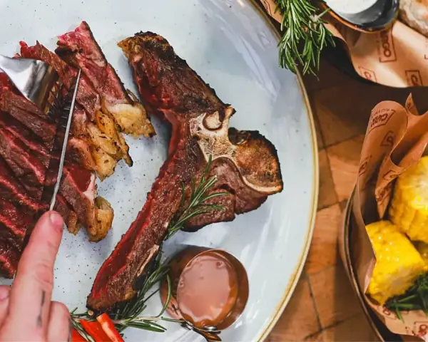 Idealne jakie wino do steka? Soczysty stek T-bone z pieczonymi kolbami kukurydzy i sosem.