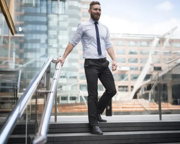 Uomo con pantaloni neri come abbinarli: camicia azzurra e cravatta blu, un look da ufficio moderno.