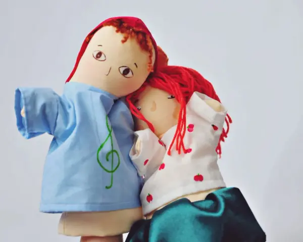 Dwie przytulone lalki nakładane na dłoń. Jedna w niebieskiej koszulce z kluczem wiolinowym, druga w białej z jabłuszkami.