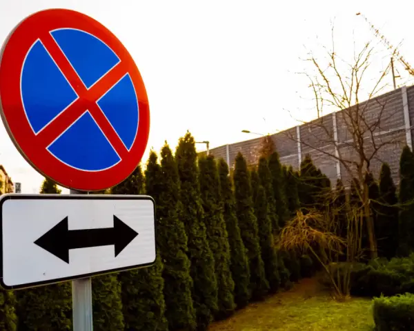Znak zakaz parkowania z tabliczką wskazującą kierunki.