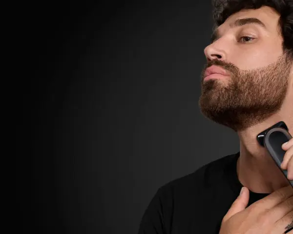 Hombre con barba cola de pato, perfil, usando una recortadora Braun para definir su estilo.