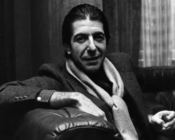 Leonard Cohen, mit Schal und Zigarette, sitzt nachdenklich auf einem Ledersofa. Ein ikonisches Bild, das den Geist des Sängers einfängt.