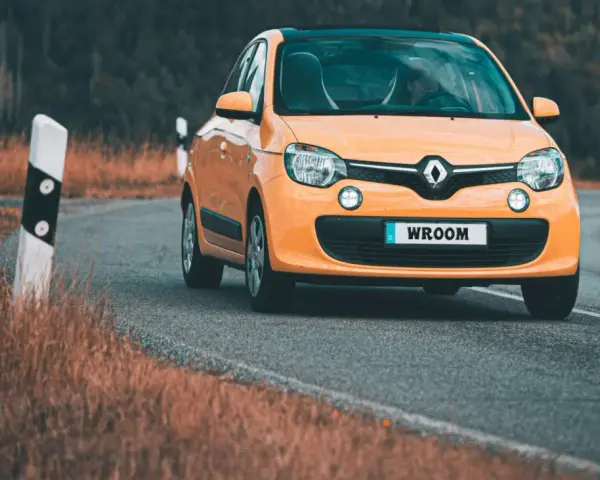 Une Twingo orange roule sur une route sinueuse bordée d'herbes sèches.