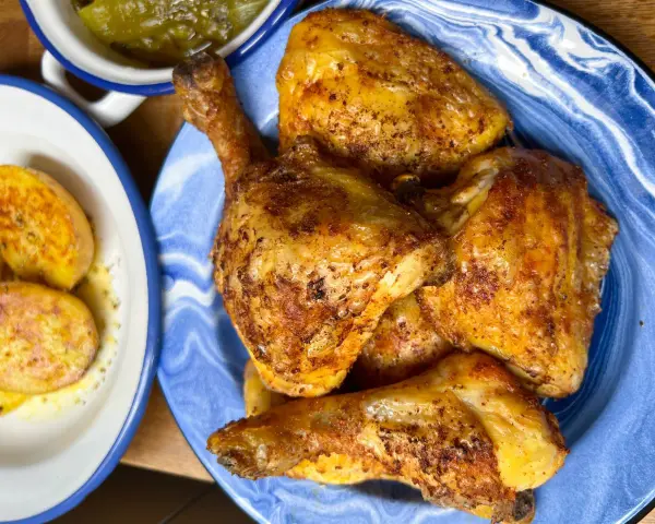 Pollo dorado y jugoso troceado en un plato azul, acompañado de patatas y pimientos.