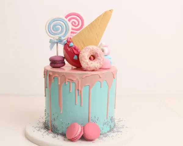 Bunter Drip Cake mit rosa Glasur, Lollis, Macarons und einem Eiswaffel-Horn.