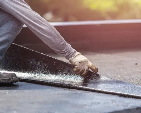Hand mit Handschuh legt neue Dachpappe an. Alte Dachpappe entsorgen ist der nächste Schritt.