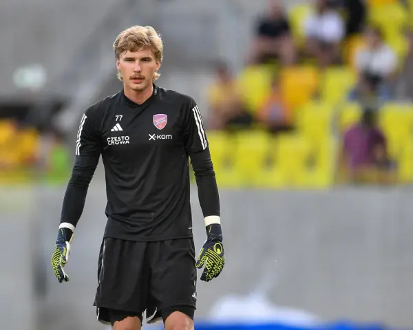Mateusz Zych, bramkarz w czarnej koszulce z numerem 77, gotowy do akcji na boisku.