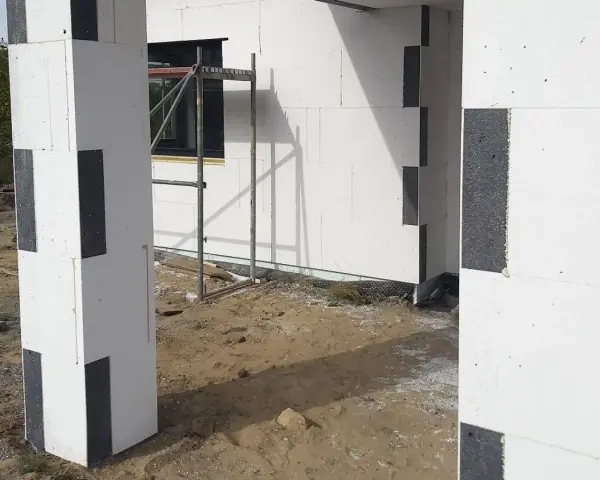 Budowa domu z bloczków styropianowych. Czy trzeba kołkować styropian grafitowy? Widok na fragment ściany i słupa z szarego styropianu.