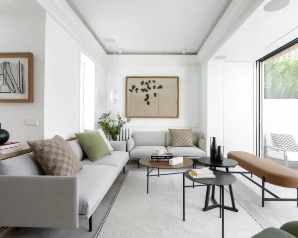 Salón moderno con sofás grises, mesas bajas negras y marrones, y un banco de cuero. Grandes ventanales conectan el interior con la terraza, creando un espacio fluido para unir terraza y salón.